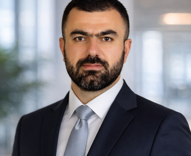 Professional headshot of a bearded man in a dark suit and tie against a blurred background