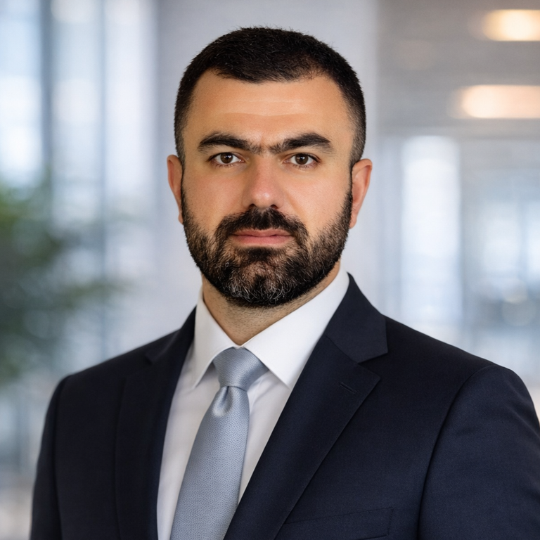Professional headshot of a bearded man in a dark suit and tie against a blurred background